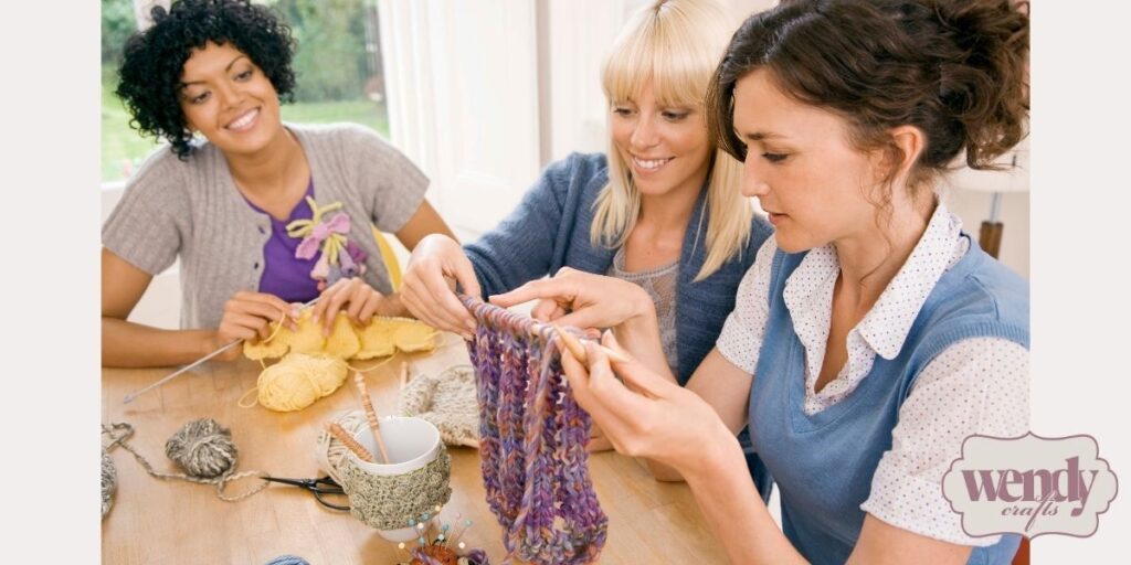 Three women sitting together and supporting one another while working on yarn crafts.