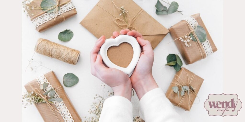 Unidentified person holding a heart-shaped craft with paper-wrapped gifts in the background.